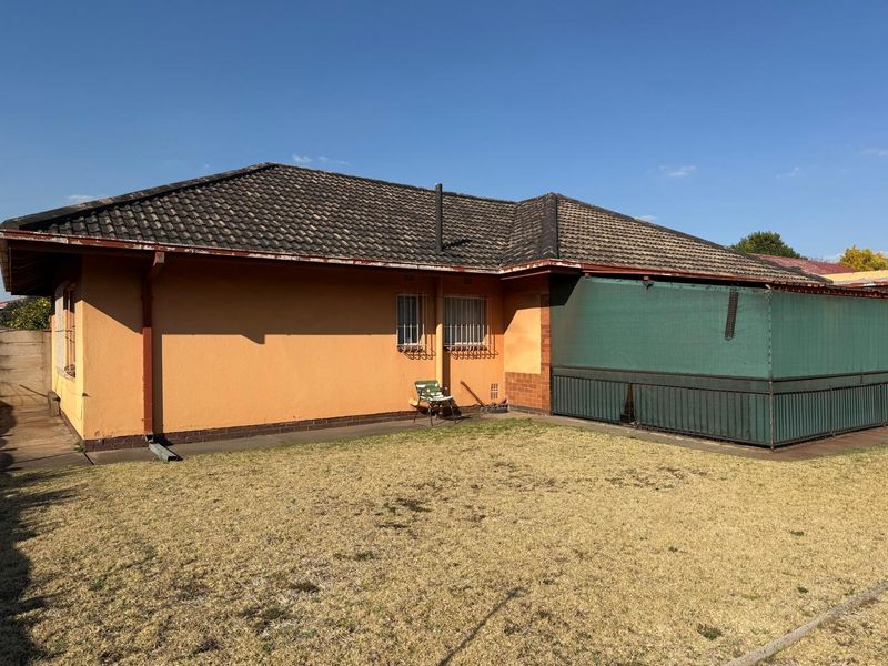 Rear view of the house featuring a tiled roof, security bars on windows, and a small lawn area with a metal-fenced patio section.