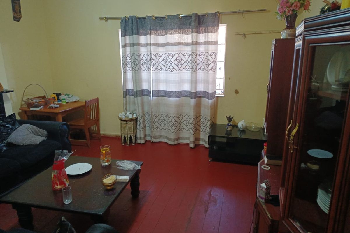 A living room featuring timber flooring and a window, currently showing signs of wear and dated finishes.