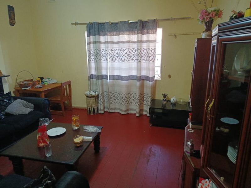 A living room featuring timber flooring and a window, currently showing signs of wear and dated finishes.