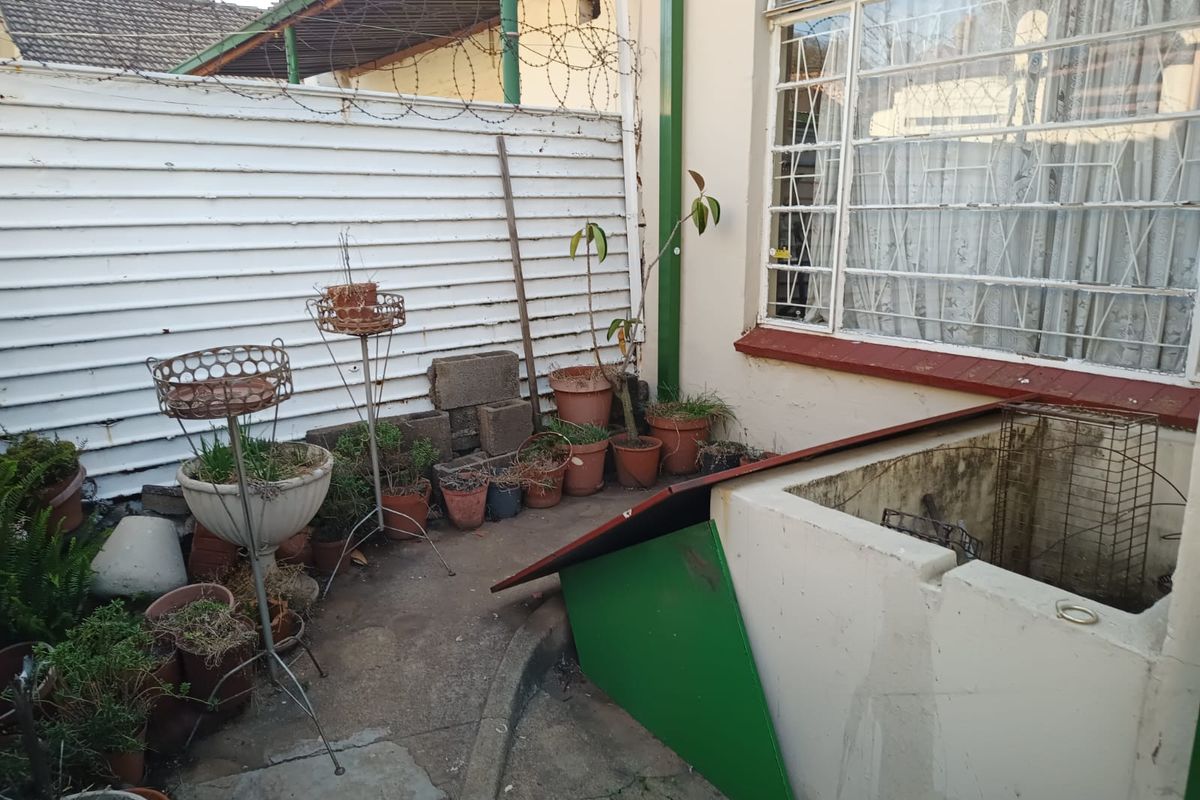 Rear exterior area featuring concrete paving, security fencing with razor wire, and steel-framed windows with burglar bars.