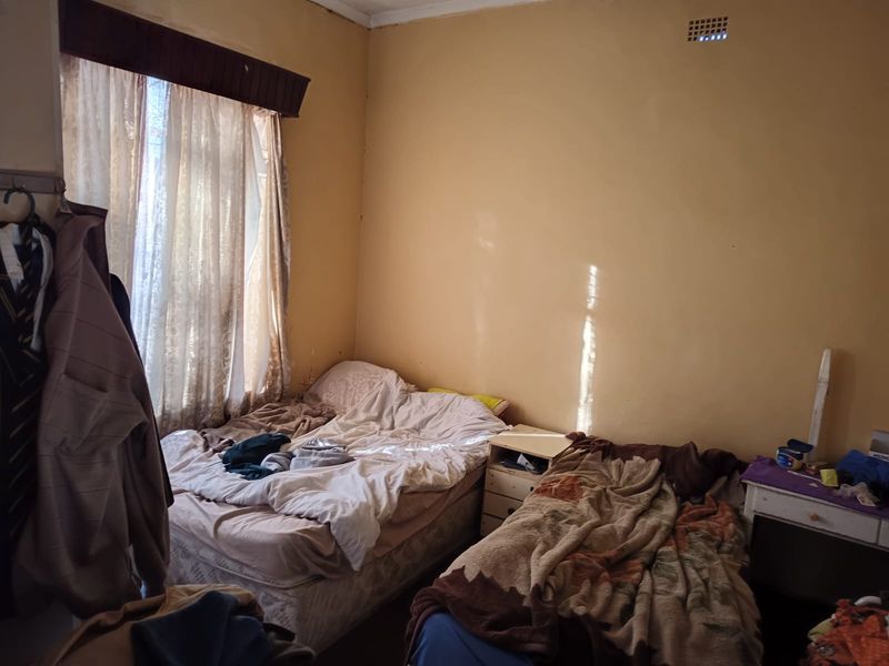 A bedroom featuring a window with curtain rails and a wall-mounted air vent, requiring cosmetic updates to the wall finishes.