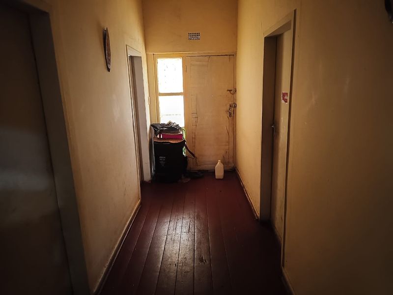 A narrow interior hallway featuring dark timber flooring and multiple internal door access points, requiring cosmetic updates to improve the overall aesthetic.