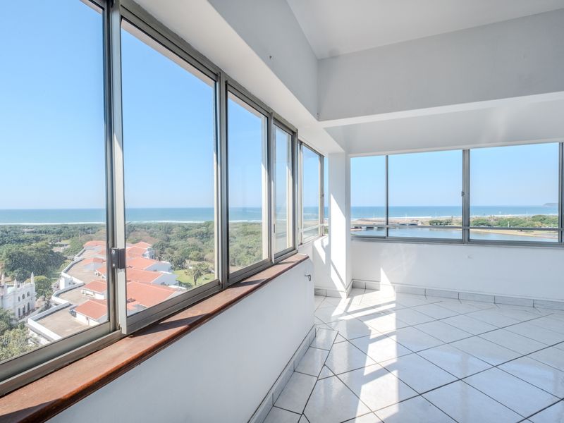 An enclosed balcony featuring tiled flooring and expansive aluminium windows offering panoramic coastal and landscape views.