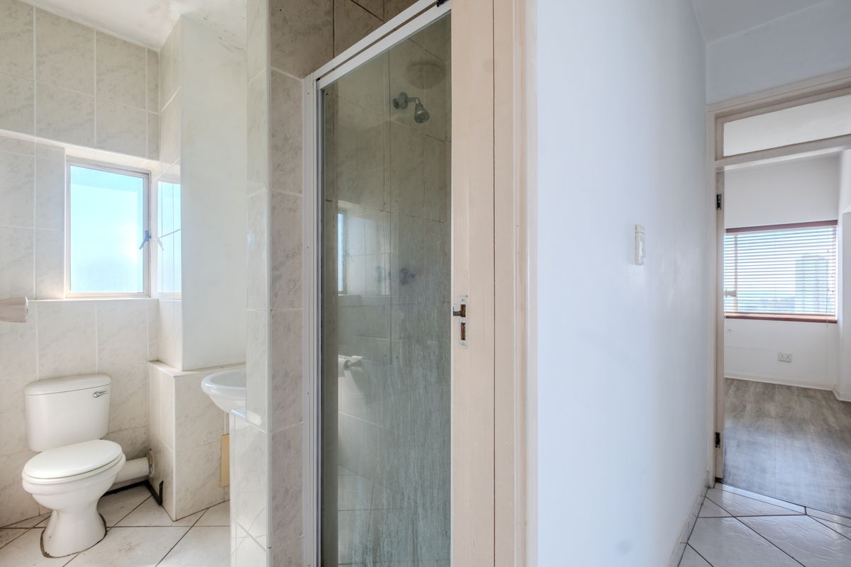 A functional bathroom featuring a shower enclosure, pedestal basin, and toilet with neutral tiled finishes, presenting a clean but dated aesthetic.