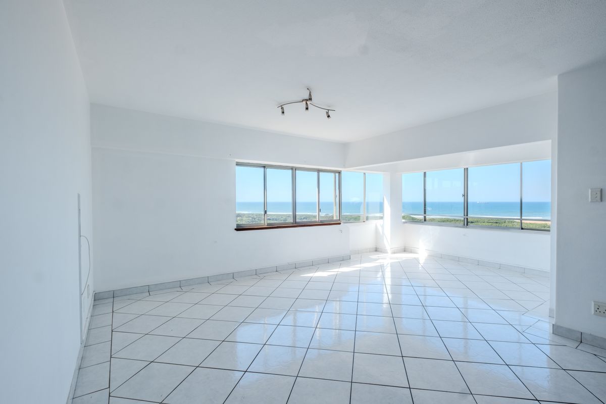 A bright, empty living area featuring white tiled floors and expansive windows offering panoramic ocean views.