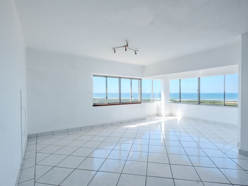 A bright, empty living area featuring white tiled floors and expansive windows offering panoramic ocean views.