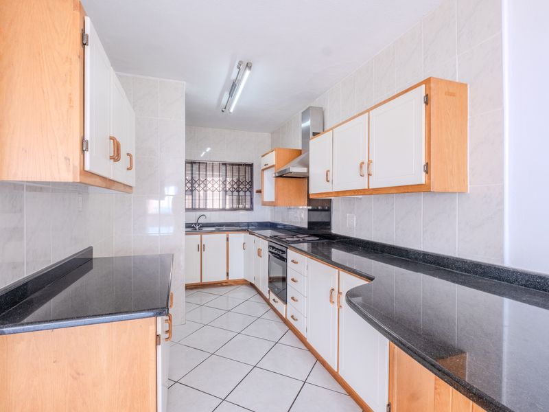 A functional galley-style kitchen featuring light wood cabinetry, dark granite countertops, built-in oven, extractor fan, and tiled finishes throughout.
