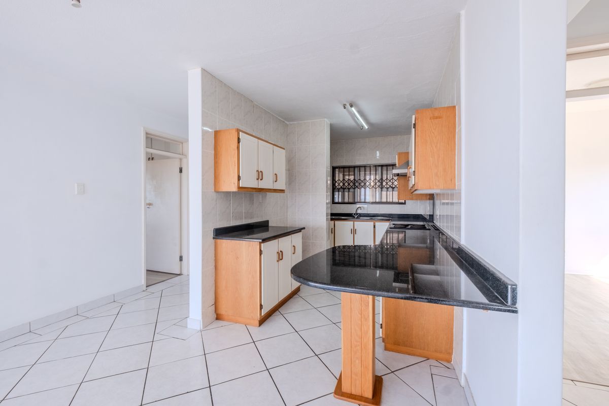 A functional kitchen featuring light wood cabinetry, dark granite countertops, a breakfast bar, and tiled flooring throughout.