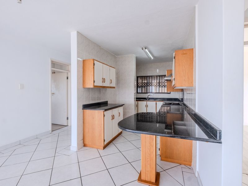 A functional kitchen featuring light wood cabinetry, dark granite countertops, a breakfast bar, and tiled flooring throughout.