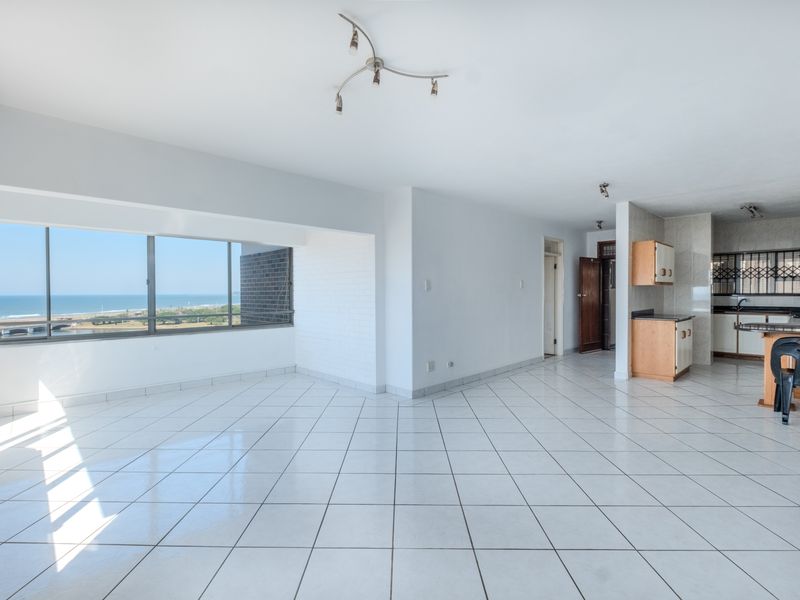 Spacious open-plan living and kitchen area featuring white tiled floors, ample natural light, and expansive ocean views through a large window.