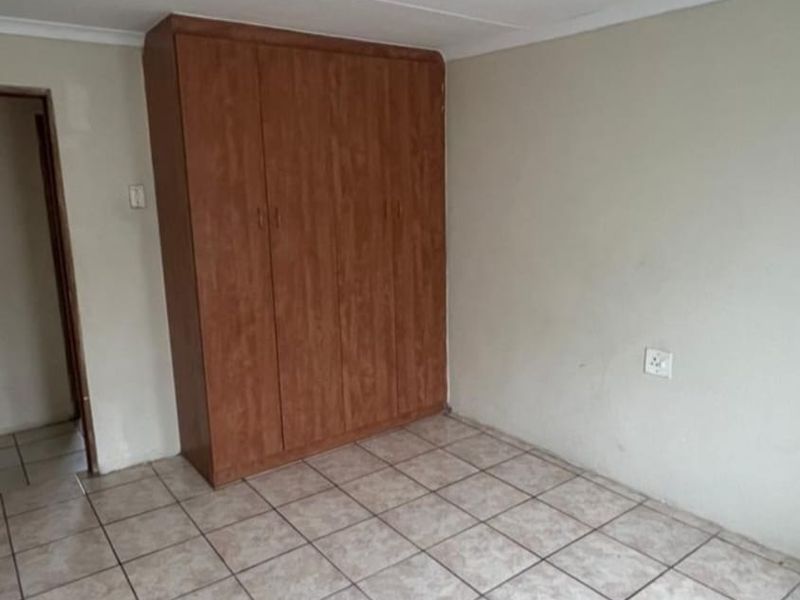 A clean, empty bedroom featuring neutral ceramic floor tiles, a built-in wooden wardrobe, and a simple coved ceiling.