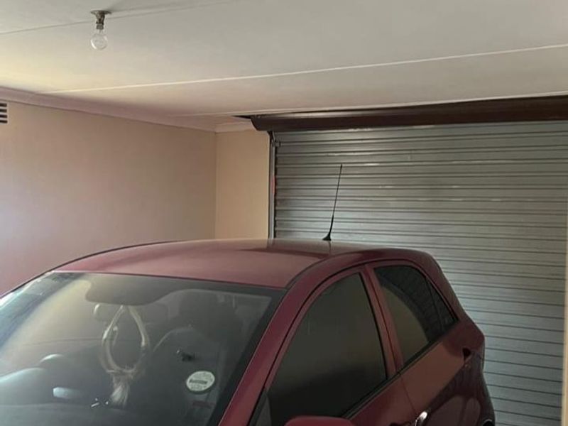A functional garage space featuring a secure roller shutter door and tiled flooring, providing covered parking.