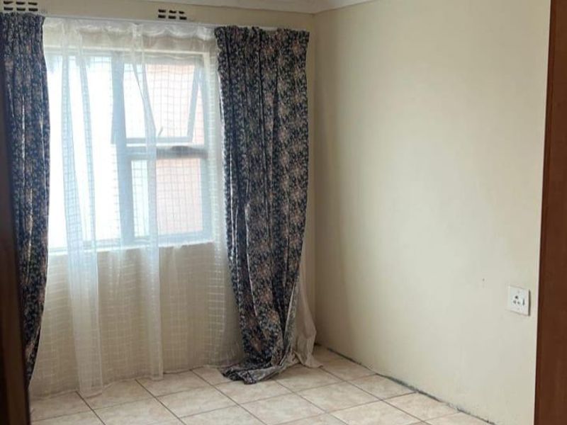 An empty bedroom featuring tiled flooring and a window with curtain tracks, offering a blank canvas for renovation or interior design updates.