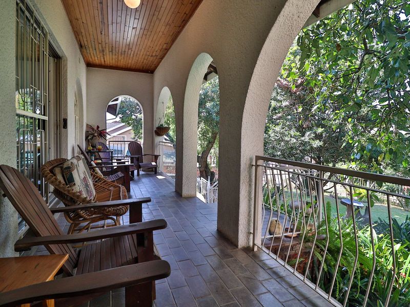 A covered patio featuring classic arched masonry columns, a warm timber-paneled ceiling, and tiled flooring, overlooking a lush garden area.