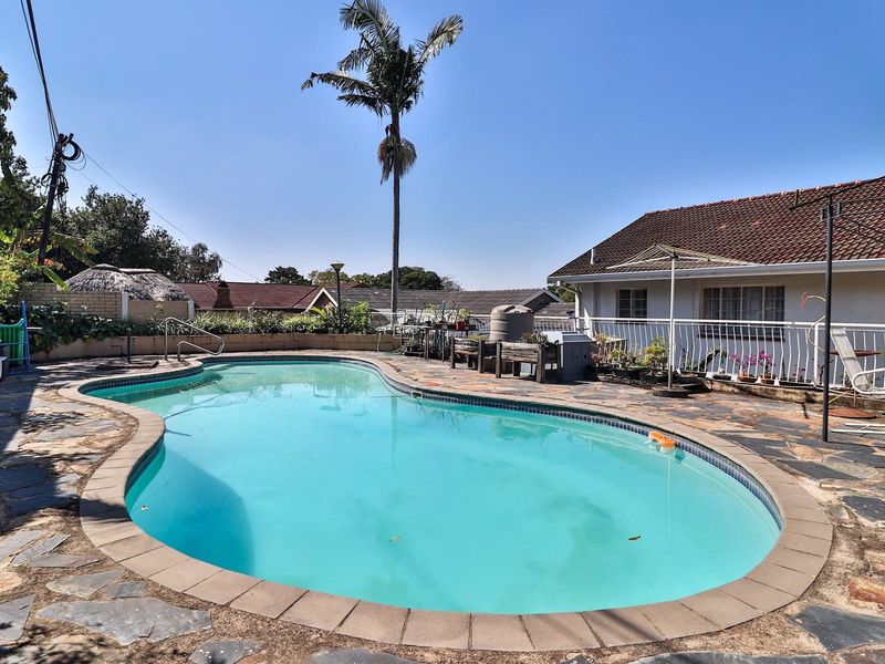 Outdoor pool area featuring a swimming pool with stone paving, a retaining wall, and access to the rear of the house.