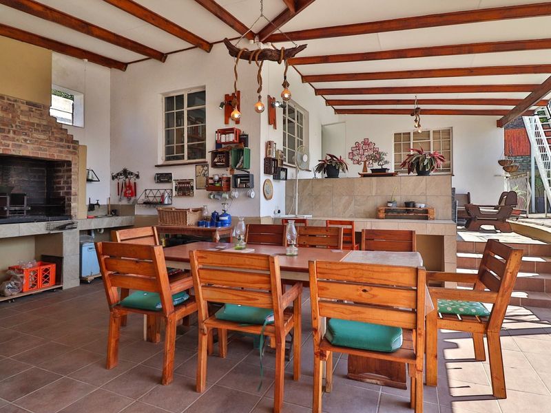 Spacious covered patio featuring a built-in brick braai, exposed timber ceiling beams, and tiled flooring, ideal for outdoor entertaining.