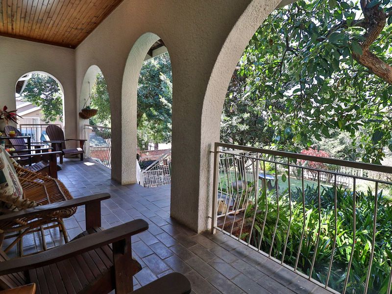 A covered patio featuring classic arched masonry columns, a warm timber ceiling, and tiled flooring, overlooking a lush garden area.