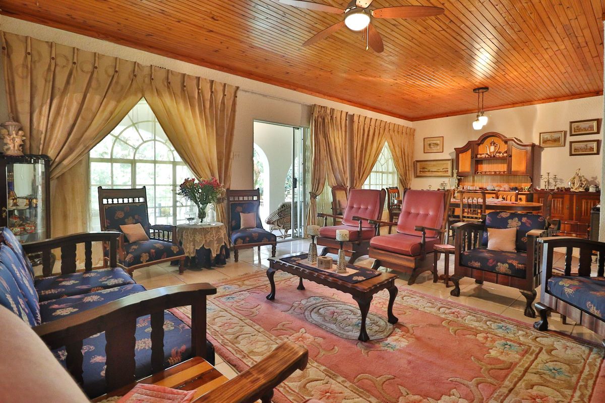 Spacious living area featuring a warm timber-clad ceiling, ceiling fan, tiled flooring, and large arched windows providing natural light and access to the patio.