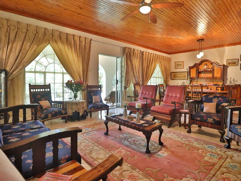Spacious living area featuring a warm timber-clad ceiling, ceiling fan, tiled flooring, and large arched windows providing natural light and access to the patio.