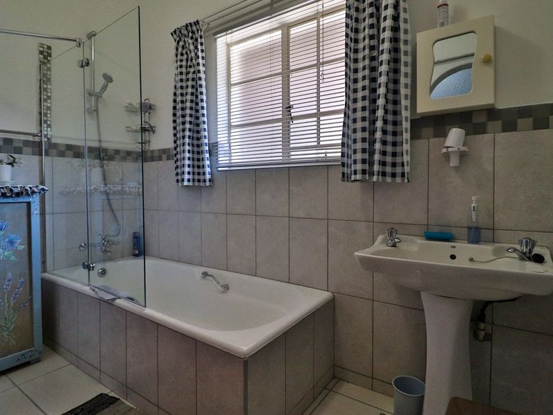A functional bathroom featuring a pedestal basin, a built-in bathtub with a glass shower screen, and neutral wall tiling.