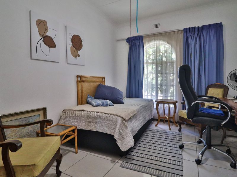 A functional bedroom featuring tiled flooring and an arched window, providing natural light and a neutral base for interior design.