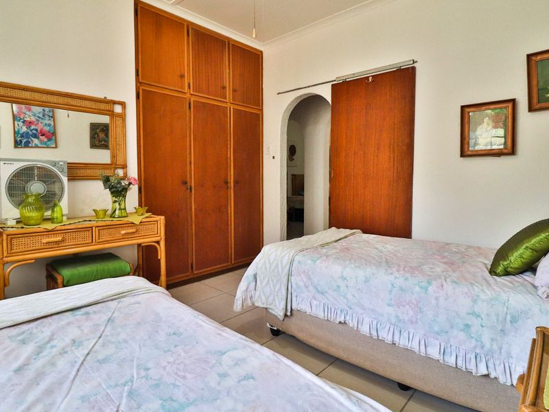 A bedroom featuring built-in wooden cupboards, tiled flooring, and an arched doorway leading to an adjacent space.