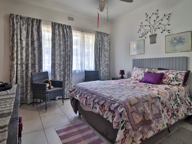 A well-lit bedroom featuring tiled flooring, a ceiling fan, and a built-in wardrobe, offering a functional and comfortable living space.