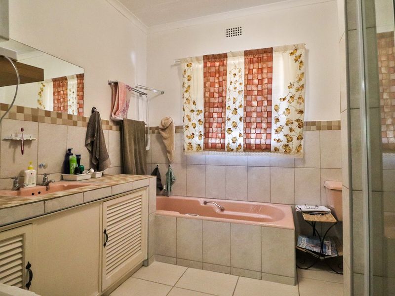 A dated bathroom featuring a built-in vanity, tiled splashback, and a classic pink bathtub with matching basin.