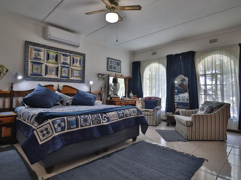 Spacious bedroom featuring tiled flooring, a ceiling fan, split-system air conditioning, and large arched windows allowing for natural light.