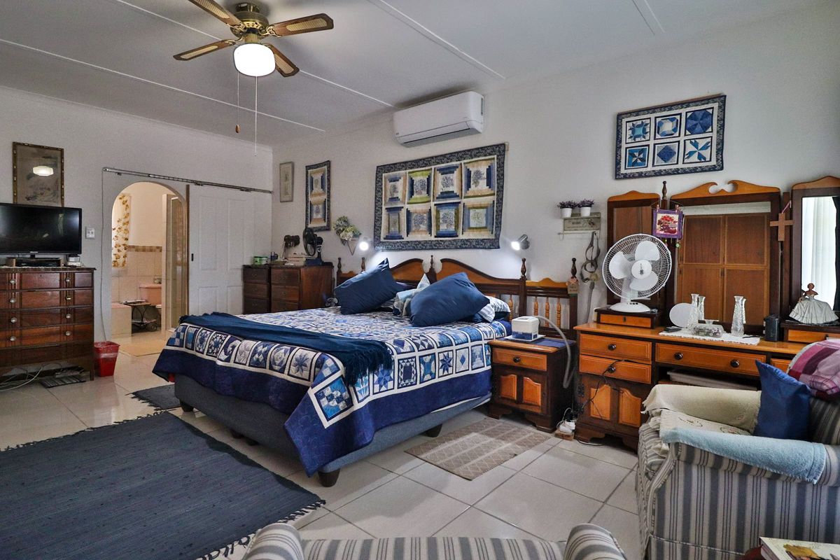 Spacious bedroom featuring tiled flooring, a ceiling fan, and a wall-mounted split-system air conditioner, with an arched doorway leading to an adjoining bathroom.
