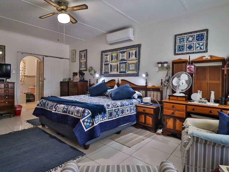 Spacious bedroom featuring tiled flooring, a ceiling fan, and a wall-mounted split-system air conditioner, with an arched doorway leading to an adjoining bathroom.