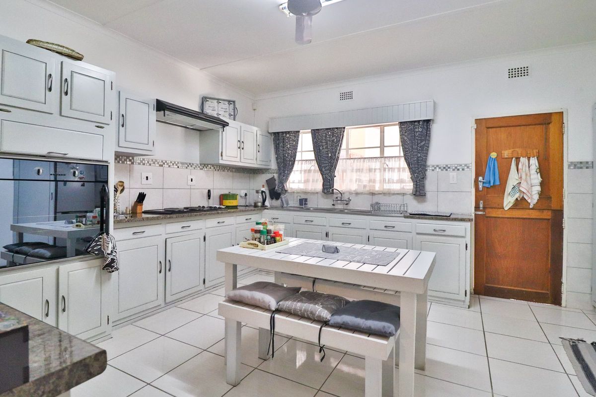 A functional kitchen featuring white cabinetry, granite countertops, built-in oven, extractor fan, and tiled flooring with a dedicated breakfast nook area.