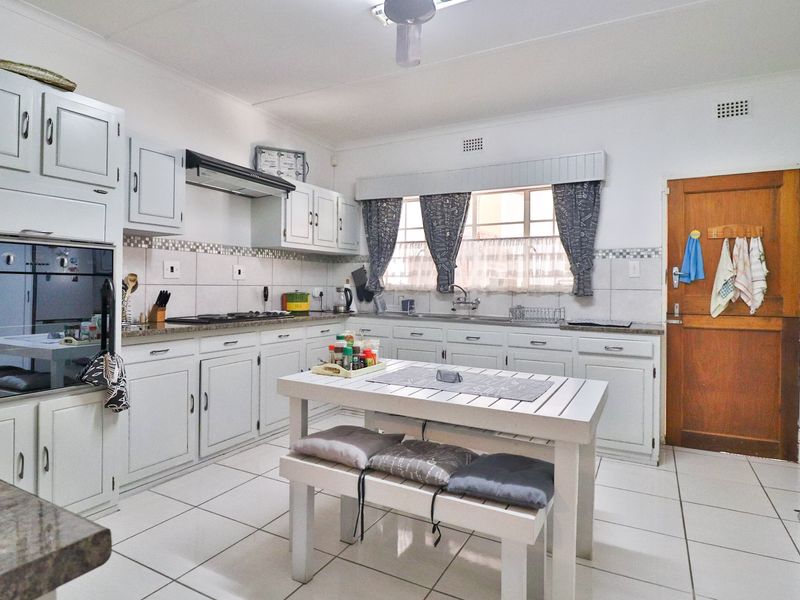 A functional kitchen featuring white cabinetry, granite countertops, built-in oven, extractor fan, and tiled flooring with a dedicated breakfast nook area.