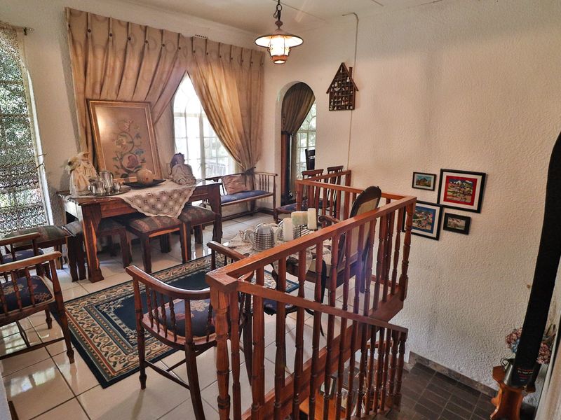 A living area featuring tiled flooring, a wooden balustrade overlooking a staircase, and an arched doorway leading to adjacent spaces.