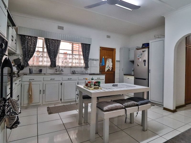 A functional kitchen featuring white built-in cabinetry, tiled flooring, a double sink, and a ceiling fan, with an arched doorway leading to adjacent spaces.