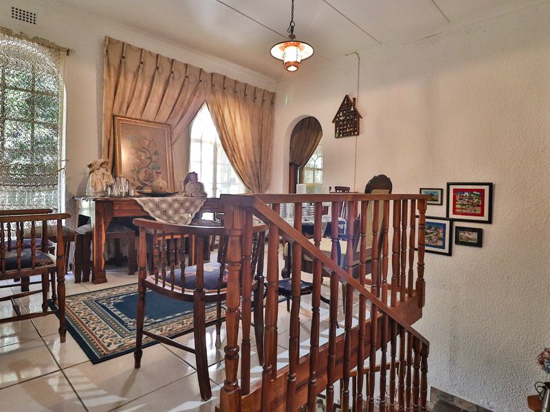 A living area featuring tiled flooring, a wooden staircase balustrade, and an arched doorway leading to adjacent spaces.