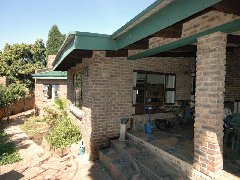 A rear exterior view featuring a face brick facade, a covered patio with tiled flooring, and a paved garden walkway.