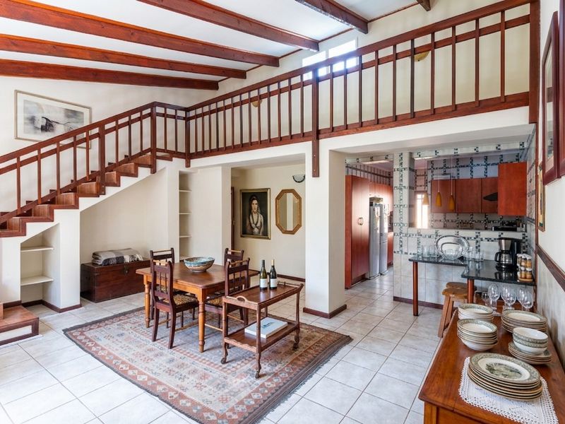 Open plan living and dining area featuring exposed timber beams, a mezzanine level with timber railing, and an adjoining kitchen with tiled finishes.