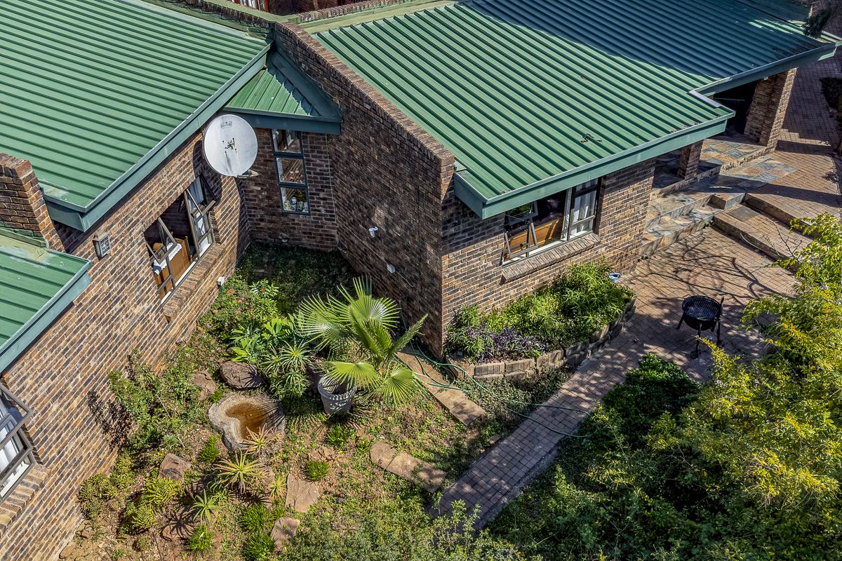 Aerial view of the rear exterior featuring a face brick facade, green corrugated metal roofing, and a paved patio area with established garden landscaping.