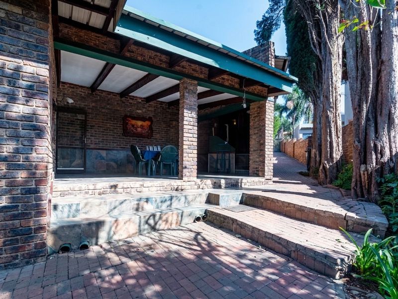 A covered outdoor patio area featuring brick construction, exposed beams, and paved steps leading to the garden.