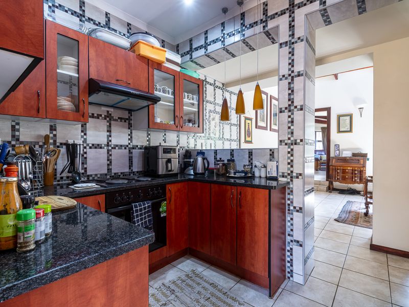 A functional kitchen featuring granite countertops, fitted wooden cabinetry, a built-in oven with hob, and a decorative tiled backsplash, opening into the living area.