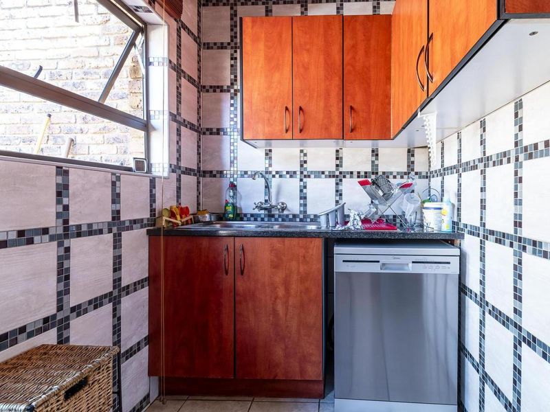A compact scullery area featuring wooden cabinetry, a stainless steel sink, and distinctive grid-patterned wall tiling.