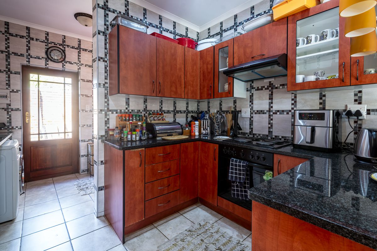 Functional kitchen featuring warm-toned wooden cabinetry, granite countertops, built-in oven, and hob, with direct access to the exterior through a timber door.