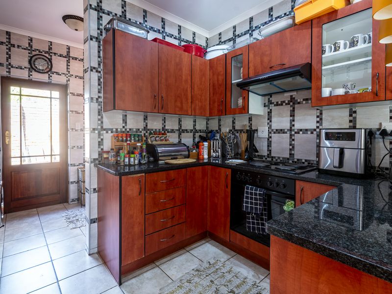 Functional kitchen featuring warm-toned wooden cabinetry, granite countertops, built-in oven, and hob, with direct access to the exterior through a timber door.