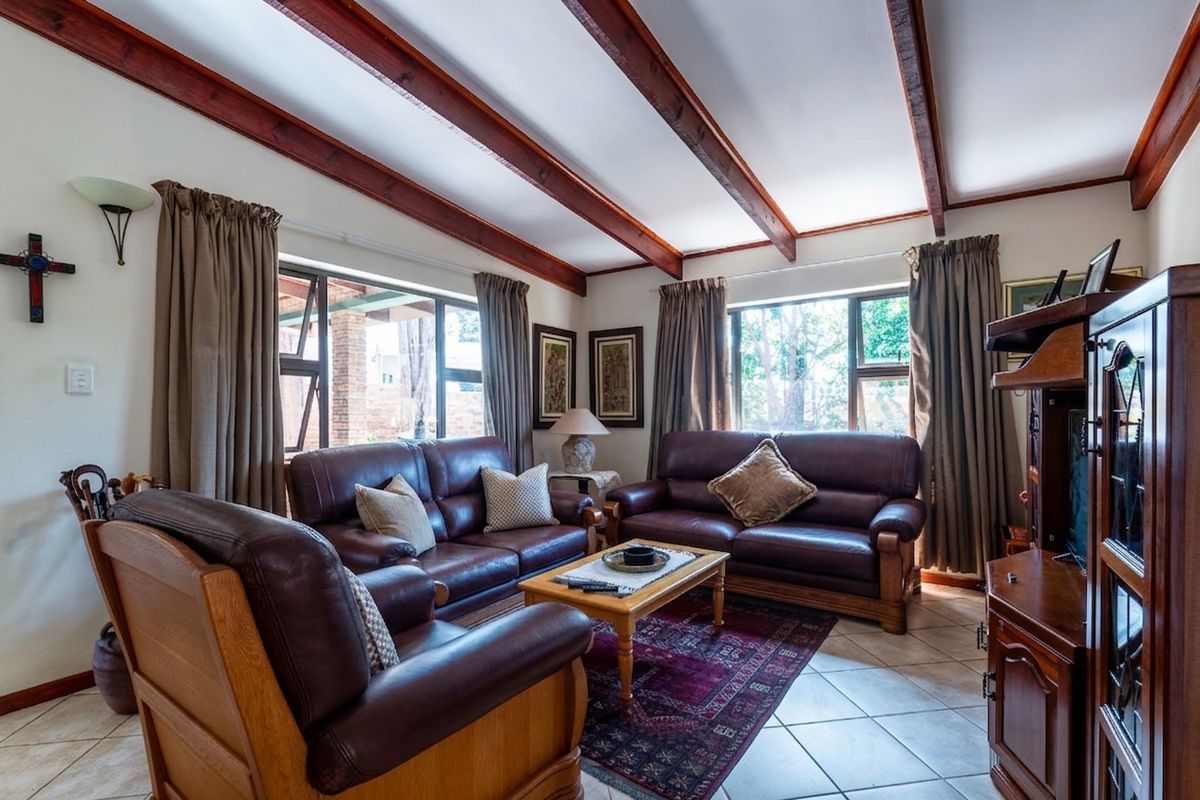 A comfortable living room featuring exposed timber ceiling beams, tiled flooring, and large windows that provide natural light.
