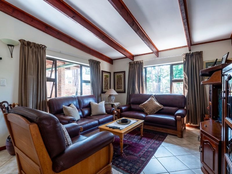 A comfortable living room featuring exposed timber ceiling beams, tiled flooring, and large windows that provide natural light.