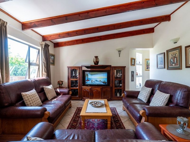 A cozy living room featuring exposed timber ceiling beams, tiled flooring, and wall sconces, offering a warm and traditional atmosphere.