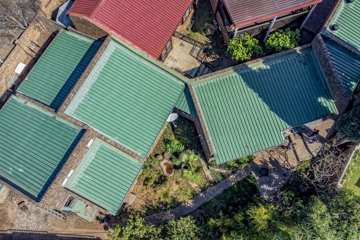 An aerial view of the property showcasing the green corrugated metal roof structure, brick exterior, and surrounding garden pathways.