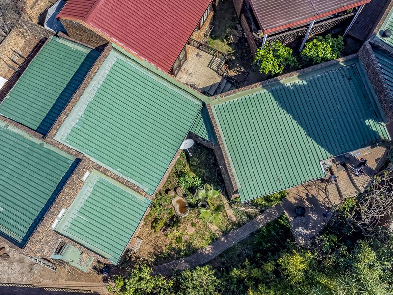 An aerial view of the property showcasing the green corrugated metal roof structure, brick exterior, and surrounding garden pathways.