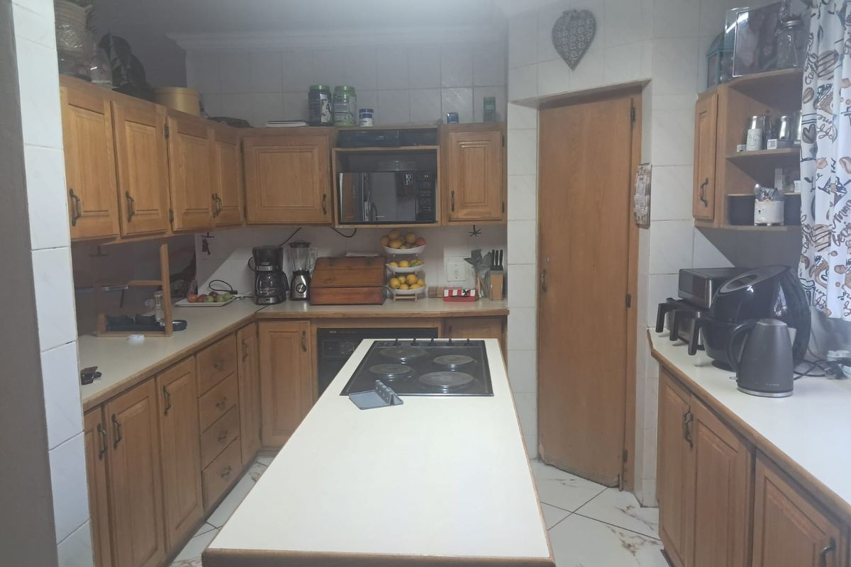 A functional kitchen featuring wooden cabinetry, a central island with a built-in electric hob, and tiled flooring throughout.